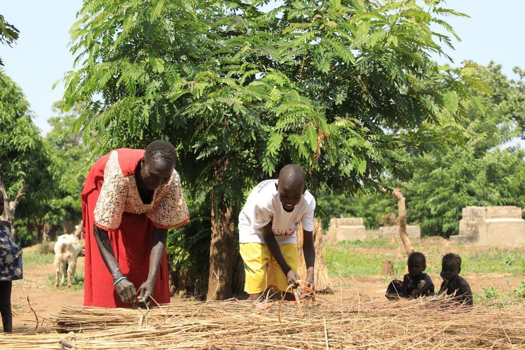 Gatwech travaille aux côtés d'un membre de sa famille pour faire des bottes de paille.