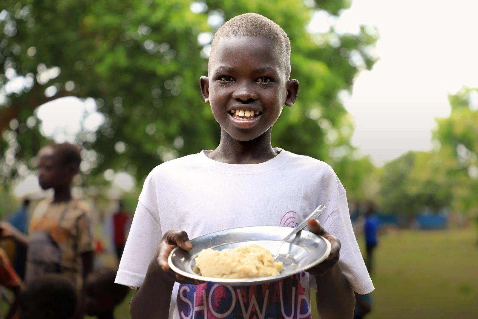 A smiling boy in Africa holds a plate of mashed potatoes.