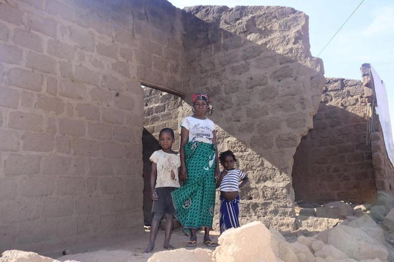 A woman and two children stand in the doorway of a roofless mud-brick home destroyed by Cyclone Chido in Cabo Delgado province, Mozambique.