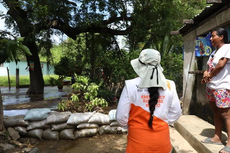 An emergency response worker speaks with a woman outside her home, where sandbags hold back floodwater after Tropical Storm John in Mexico.