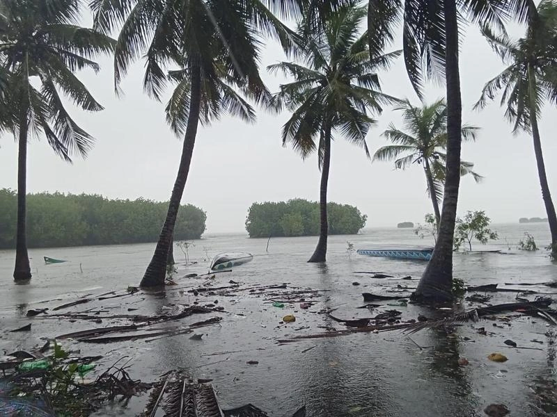 Floodwater and floating debris cover a palm-lined shoreline in Kalpitiya, Sri Lanka, with boats swept out into the water after Cyclone Ditwah.