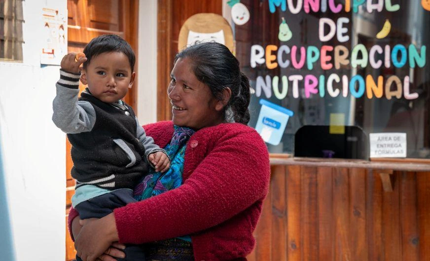 A woman smiles while holding and looking up at her son, a toddler.