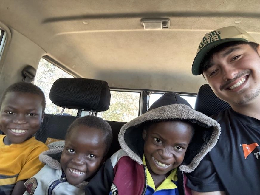 A young man takes a selfie with three younger children inside a vehicle.