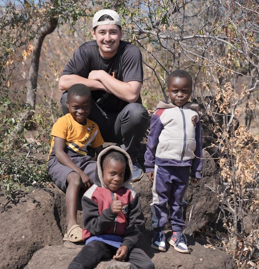 Three children pose on some rocks with a young man.