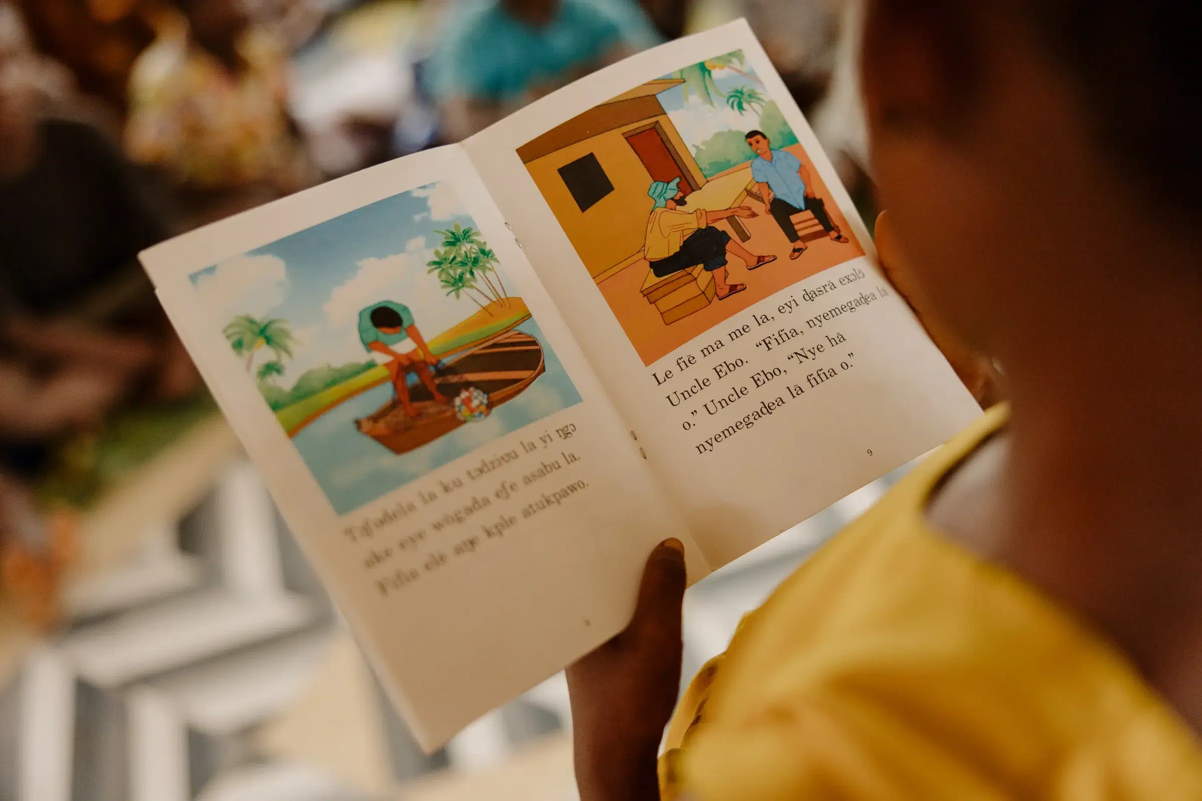 Close up of a book a young girl is reading. It's a picture book with images of a person on a boat and people sitting together.