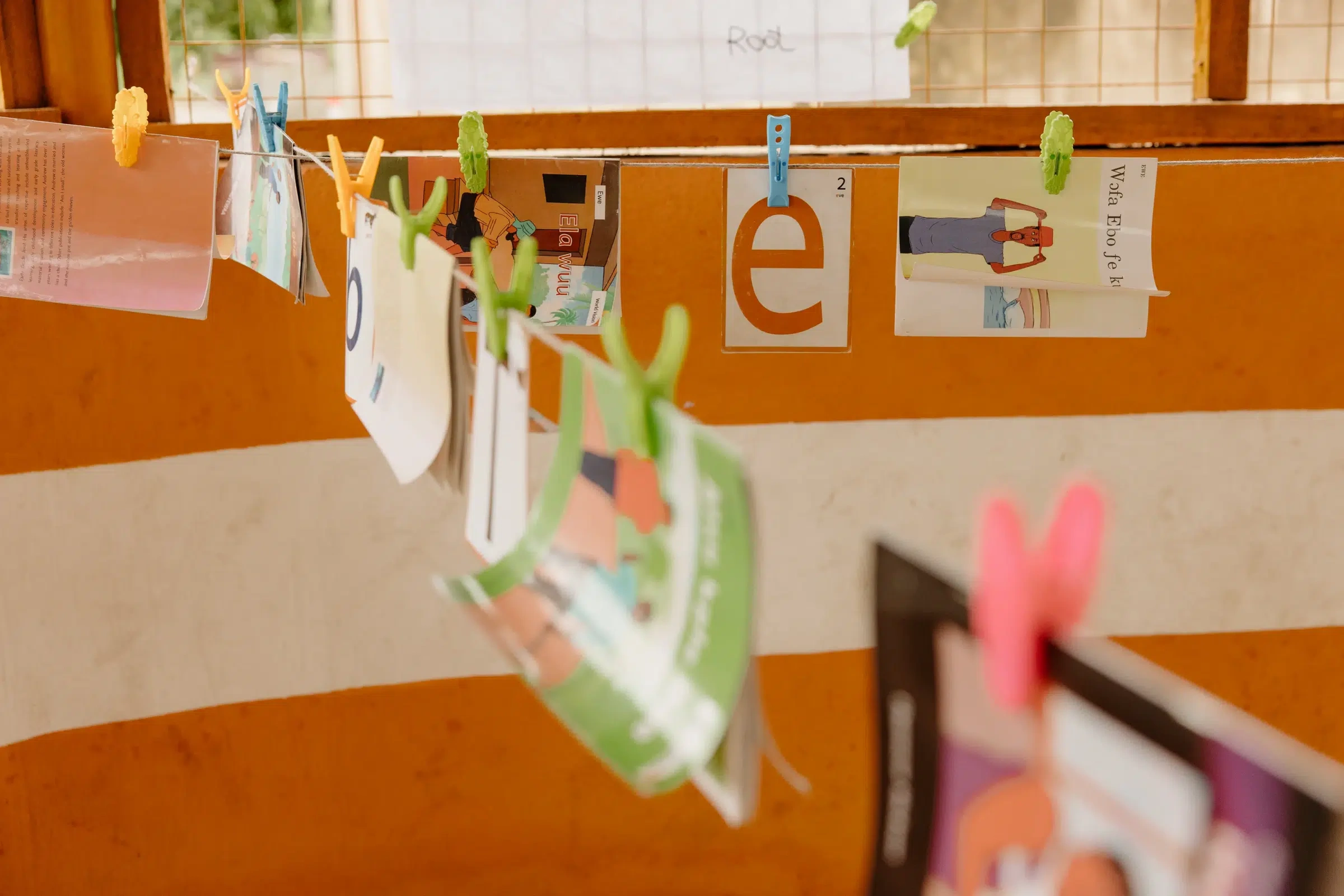 A row of colorful cards are pinned to a string by clothes pegs and hang throughout a classroom.