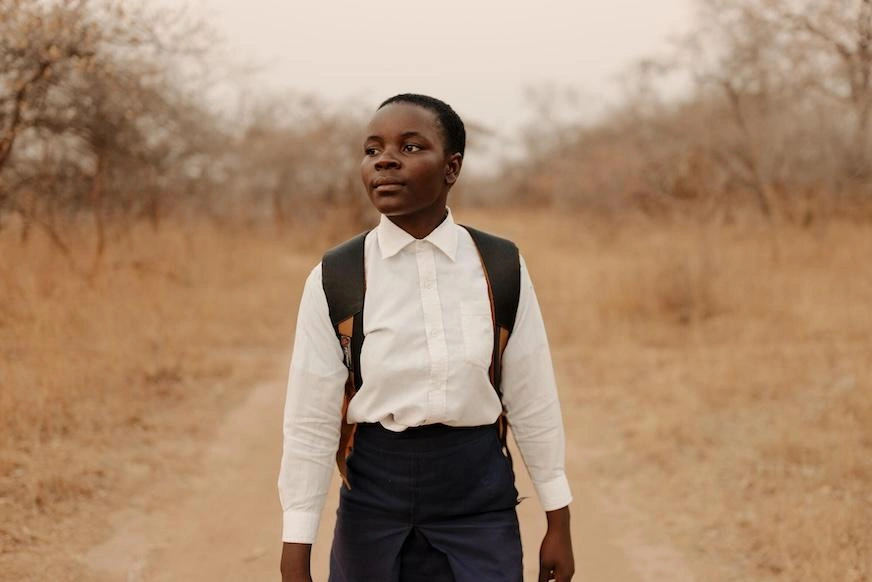 A young girl in a crisp white shirt and backpack looks into the distance while walking.