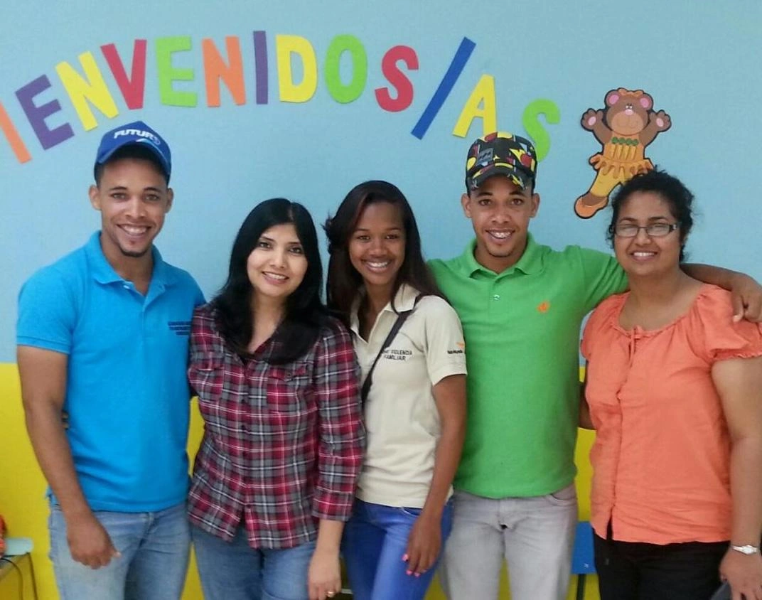 Two young men and three women pose for a photograph against a brightly decorated wall.