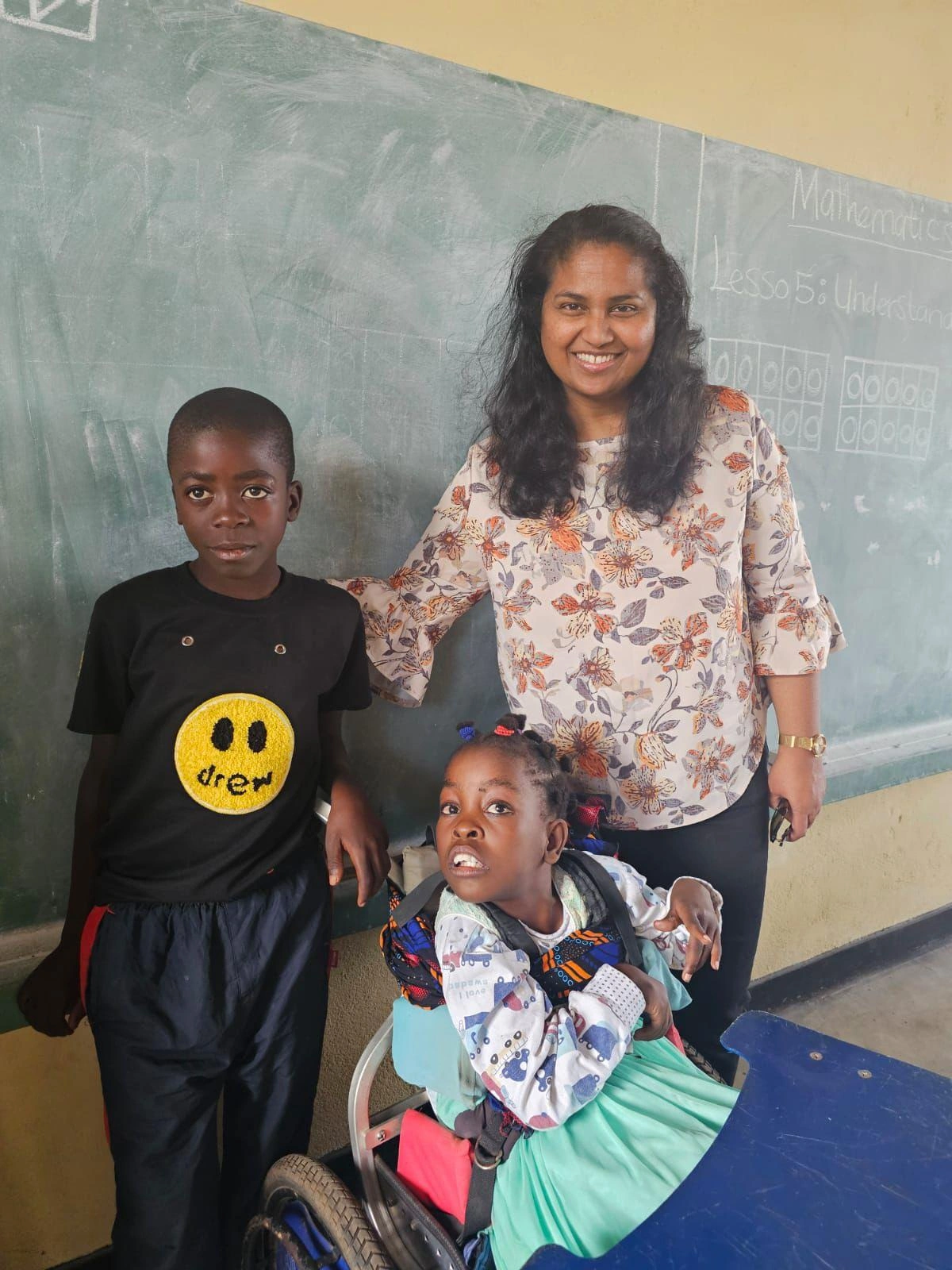 A woman stands with a boy and a girl. The girl sits in a wheelchair.