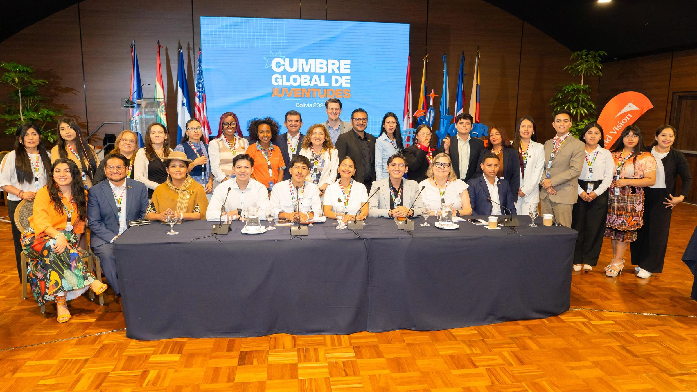A group of people stand in front of a sign and flags.