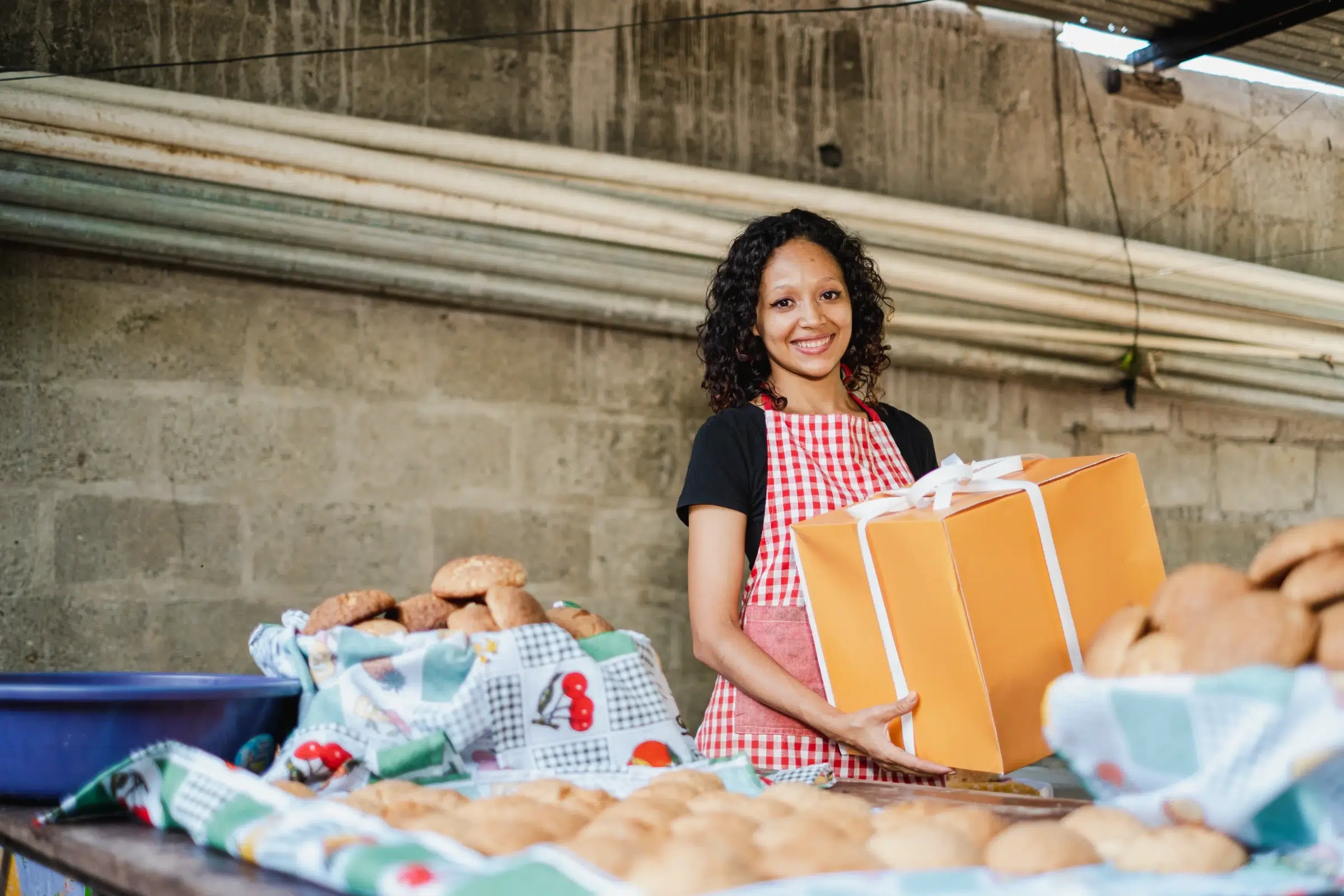 Woman smiling while holding an orange gift box for Giving Season.