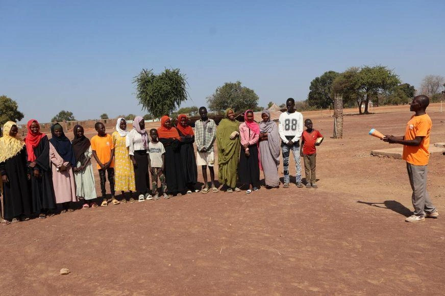 Young people standing together outdoors in a dry, open landscape while a person speaks to the group.