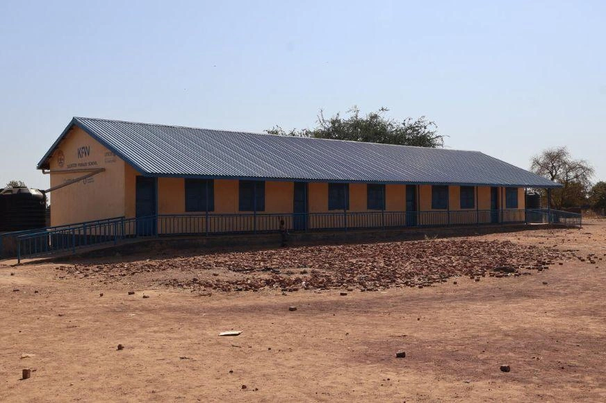 Long, single-story building with a metal roof and blue doors, surrounded by a dry, open landscape.