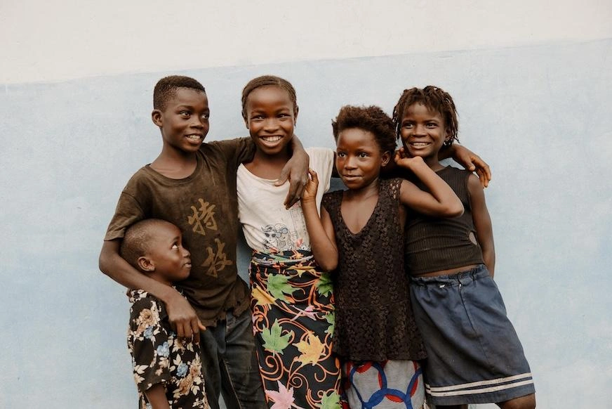 Five children stand with their arms around each other.