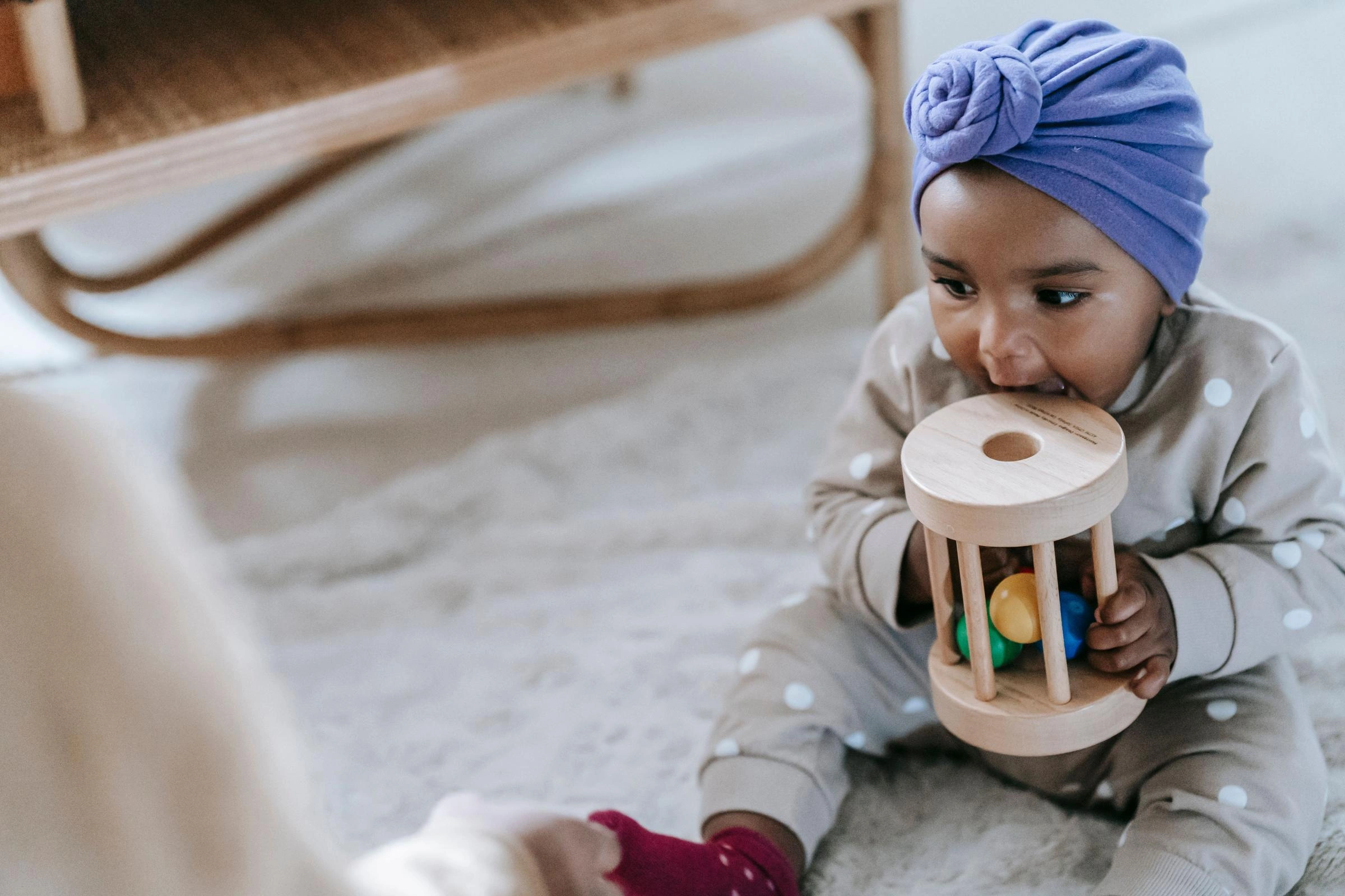 A cute baby wearing a purple headband plays with a wooden toy on a carpeted floor.