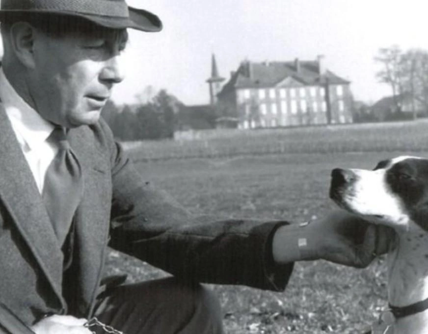 Historical image of a man in the 1940s bending down to pet a dog.