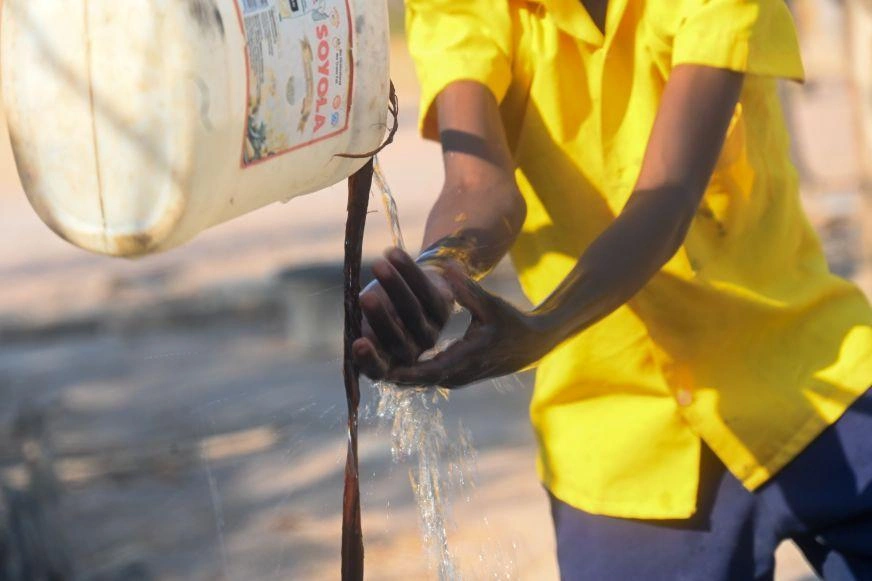 Close-up of clean water pouring onto hands from a suspended jerry can.