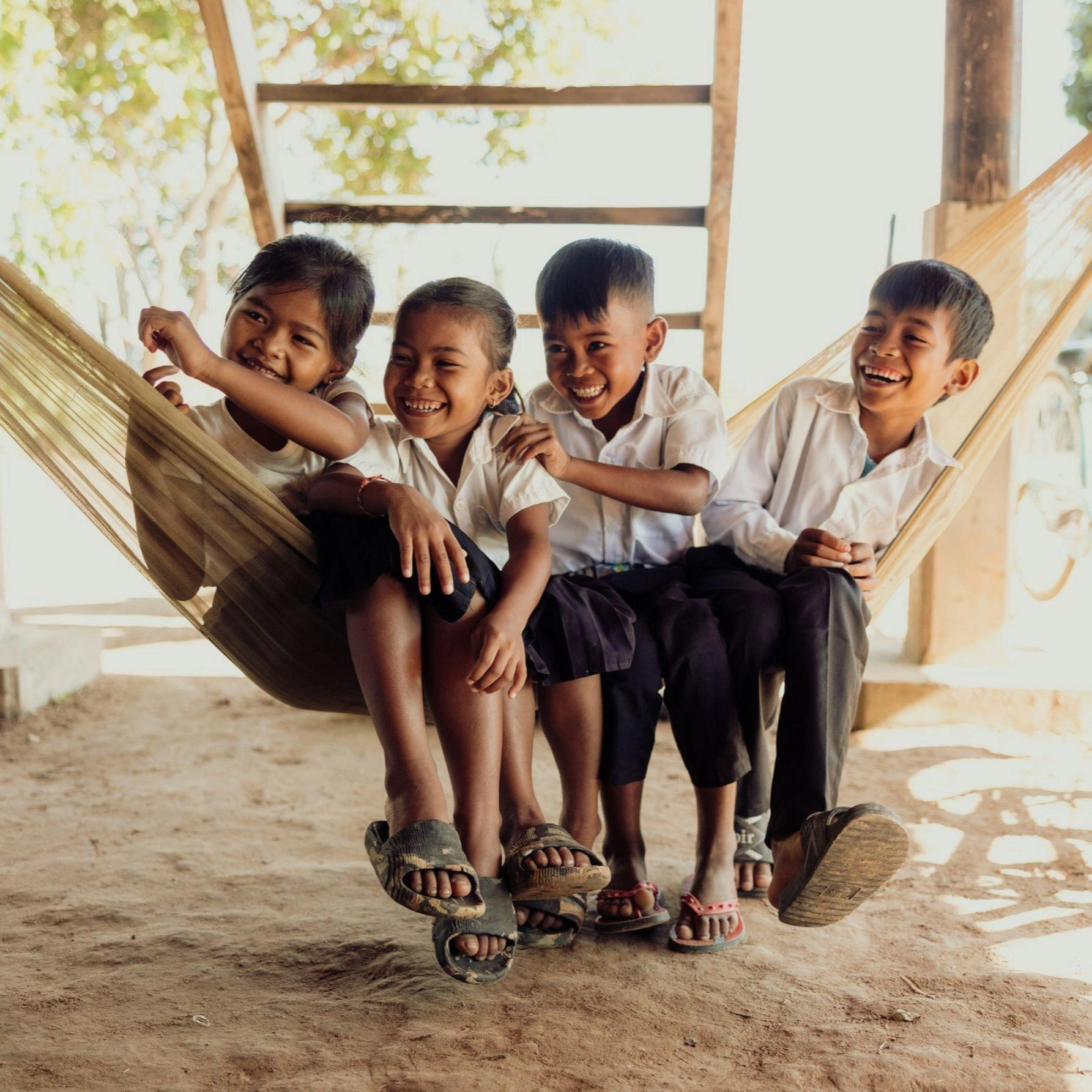 A group of children smile joyfully as they sit side by side  on a hammock.