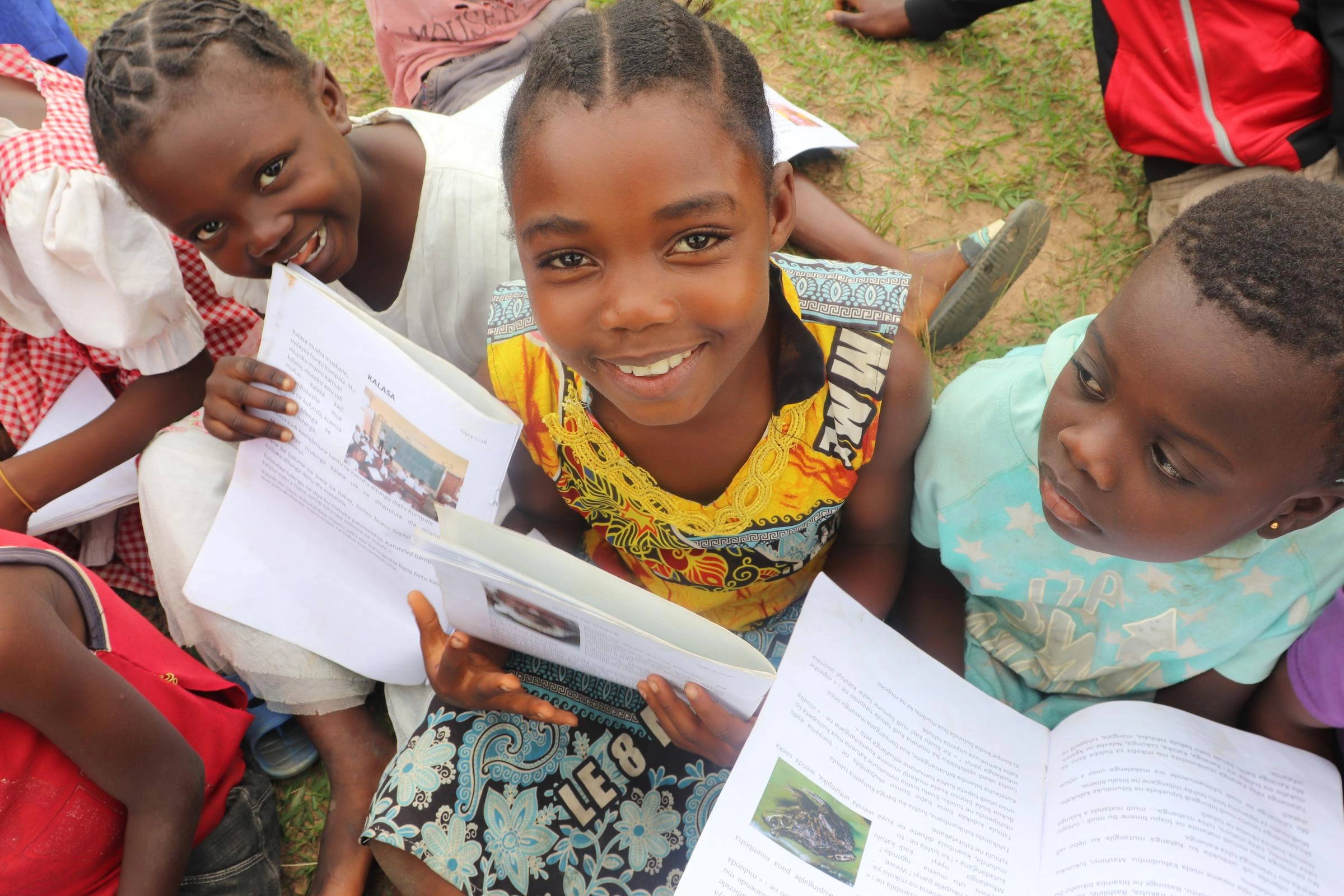 Three girls with open books. Two look at the camera, smiling.