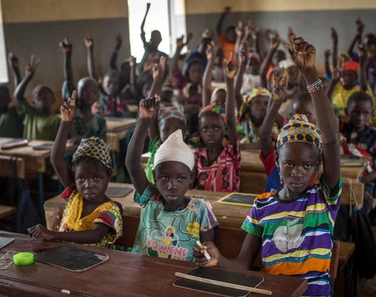 Children raise their hands in a classroom.