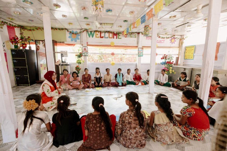 Children seated in a circle with a teacher during a classroom activity.