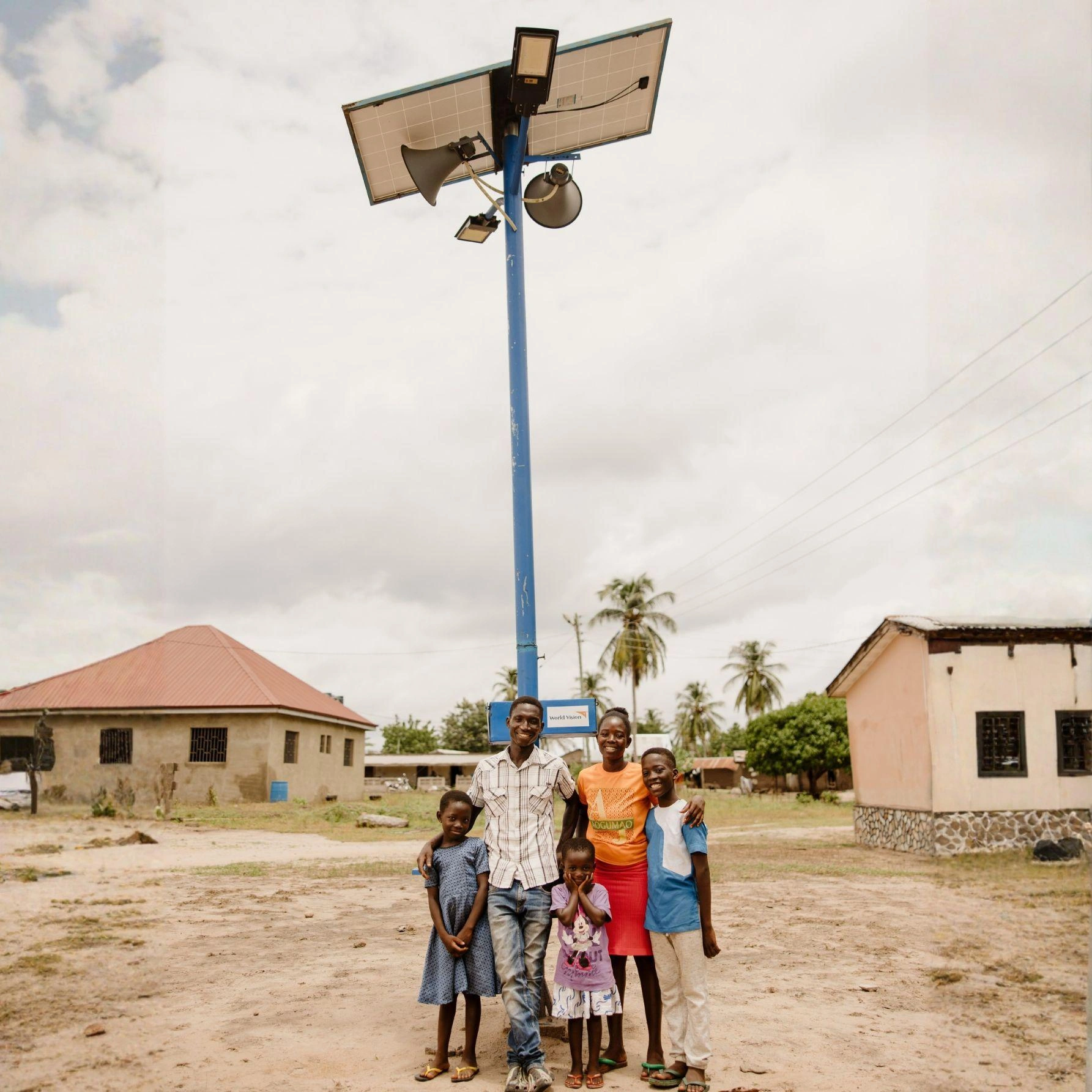 A man and woman stand in front of a multipurpose pole built by World Vision with three children.