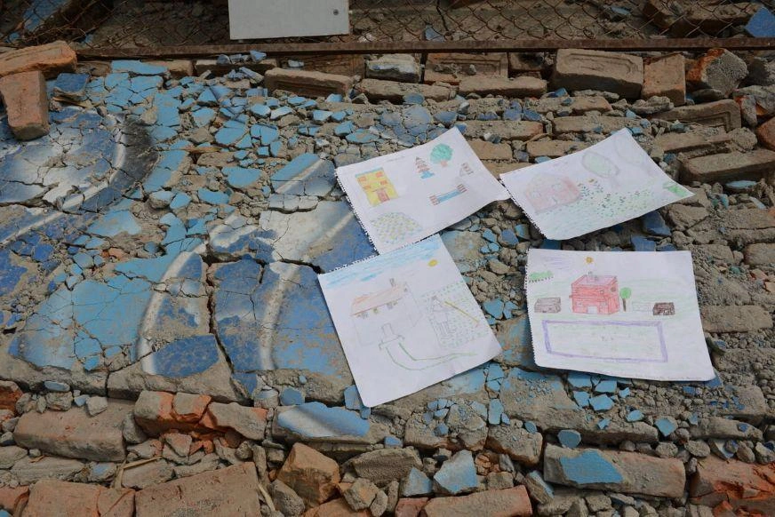 Four children’s drawings of houses lie atop cracked ceramic flooring.