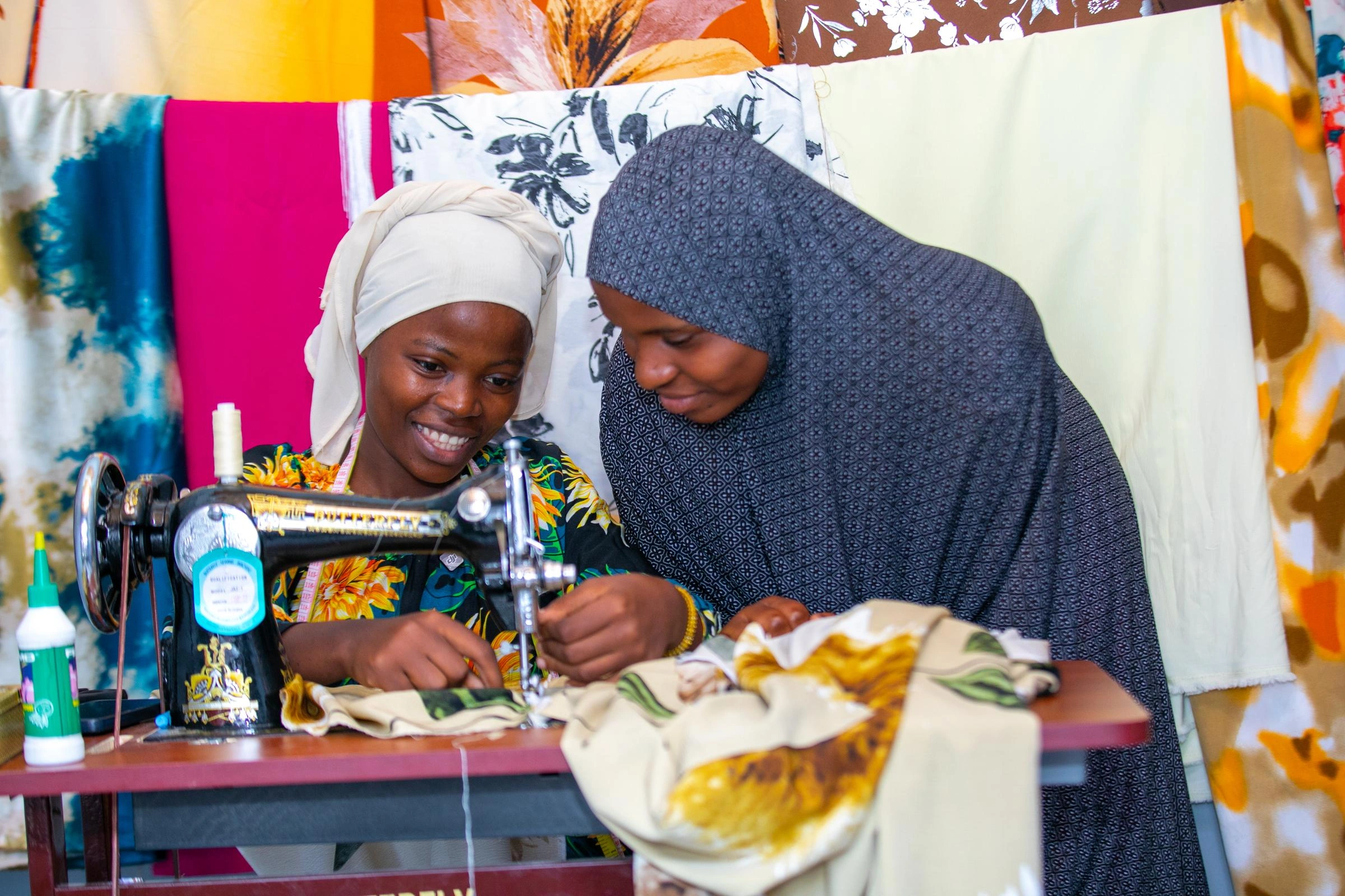 A girl uses a sewing machine, while a woman watches