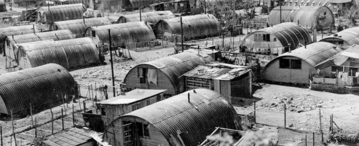 A black and white photo showing huts sitting on a muddy field in the Noisy-le-Grand camp in 1956.