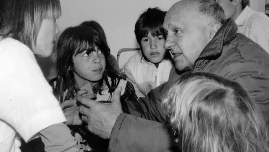 A black and white photo of Father Joseph Wresinski talking to children
