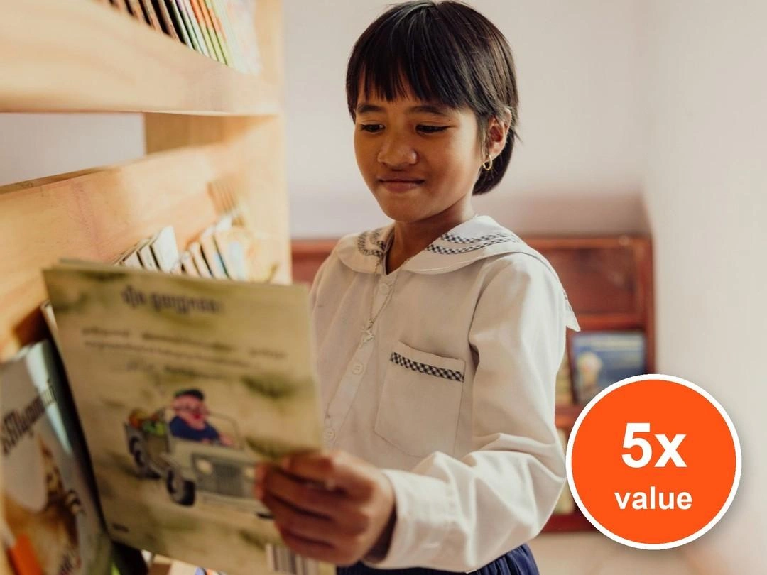 A child in white and blue uniform smiles as she holds a book. Badge: 5x value.