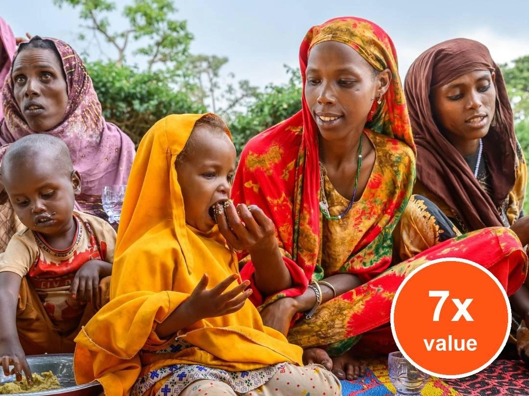 A woman wearing a red head tie feeds her daughter. Badge: 7x value.