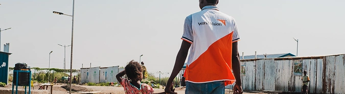 World Vision staff walks alongside young child, holding their hand.