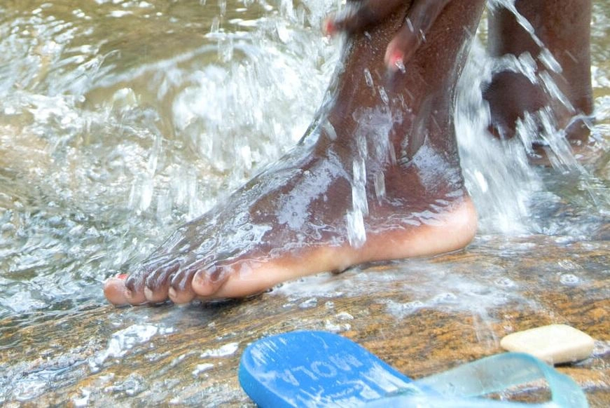 Close-up of a girl’s foot with water splashing down over it as she stands on wet rock.