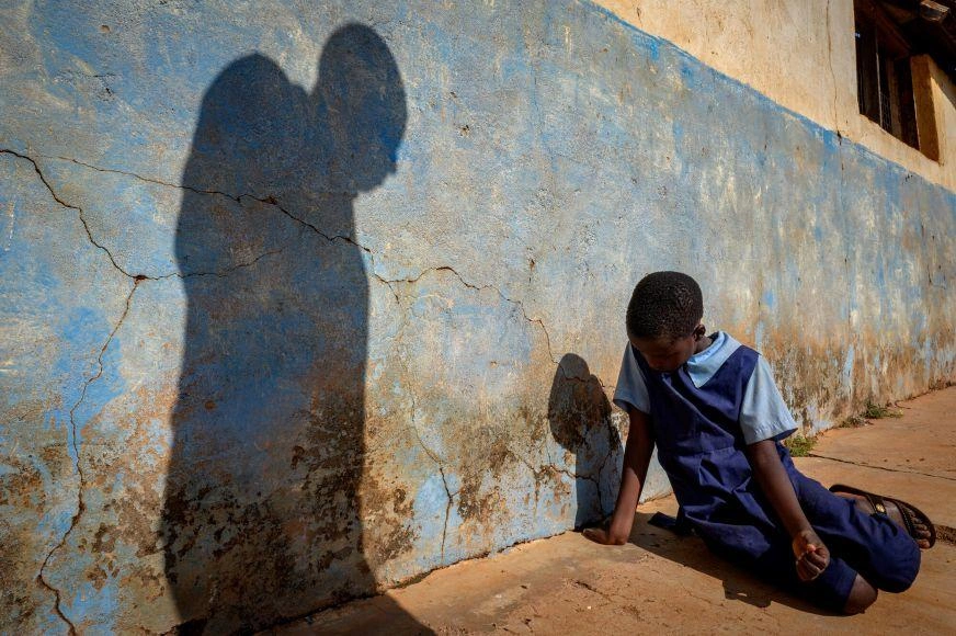 Representational photo of a girl in school uniform cowering on the ground while the shadow of a man looms over her. (