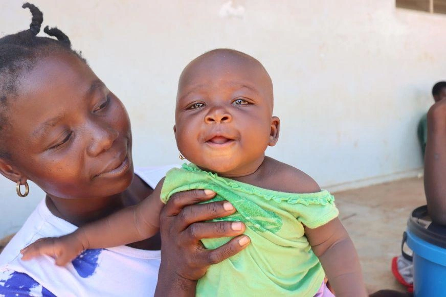 A young woman holds up a baby girl who is smiling.