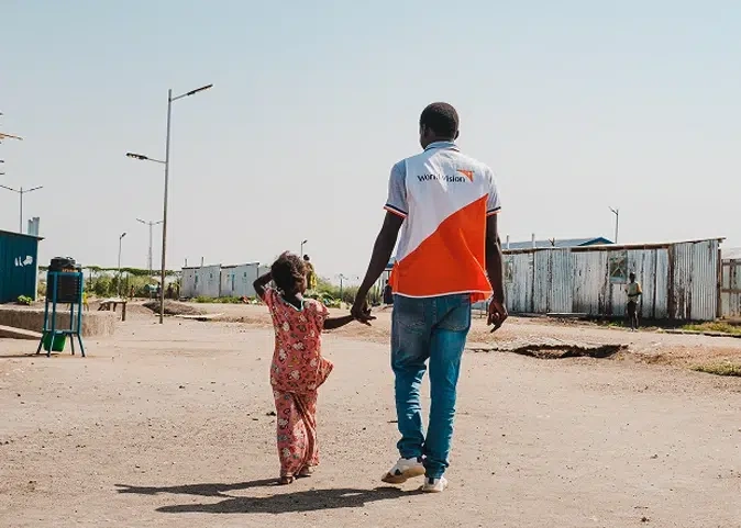 World Vision staff walks alongside young child, holding their hand.